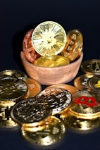 A wooden bowl filled with various golden and copper-colored cryptocurrency coins is surrounded by more coins on a dark surface. Each coin features distinct cryptocurrency symbols, including Bitcoin, Ethereum, and others.