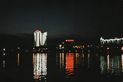 Nighttime shot of Dubai's illuminated towers reflecting on the calm waters of the bay.