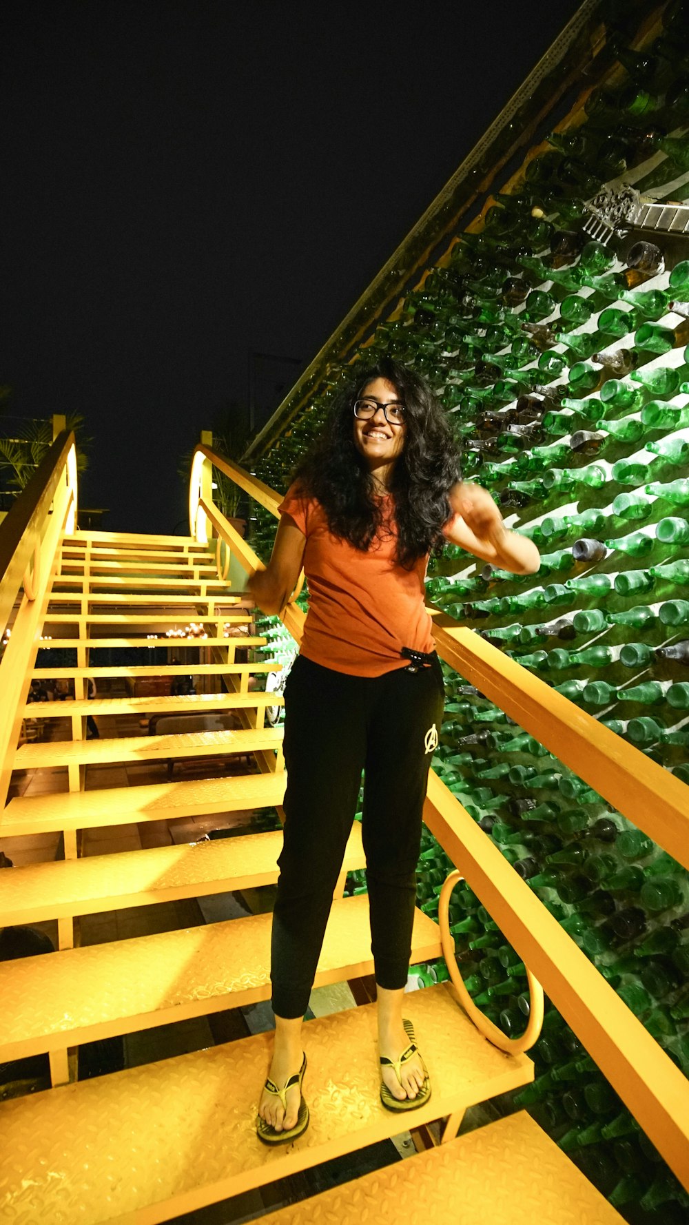 woman in brown top and black pants standing on white stair outdoors