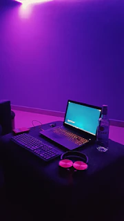 A cozy home studio corner lit by purple LED strips, with headphones resting on a keyboard.