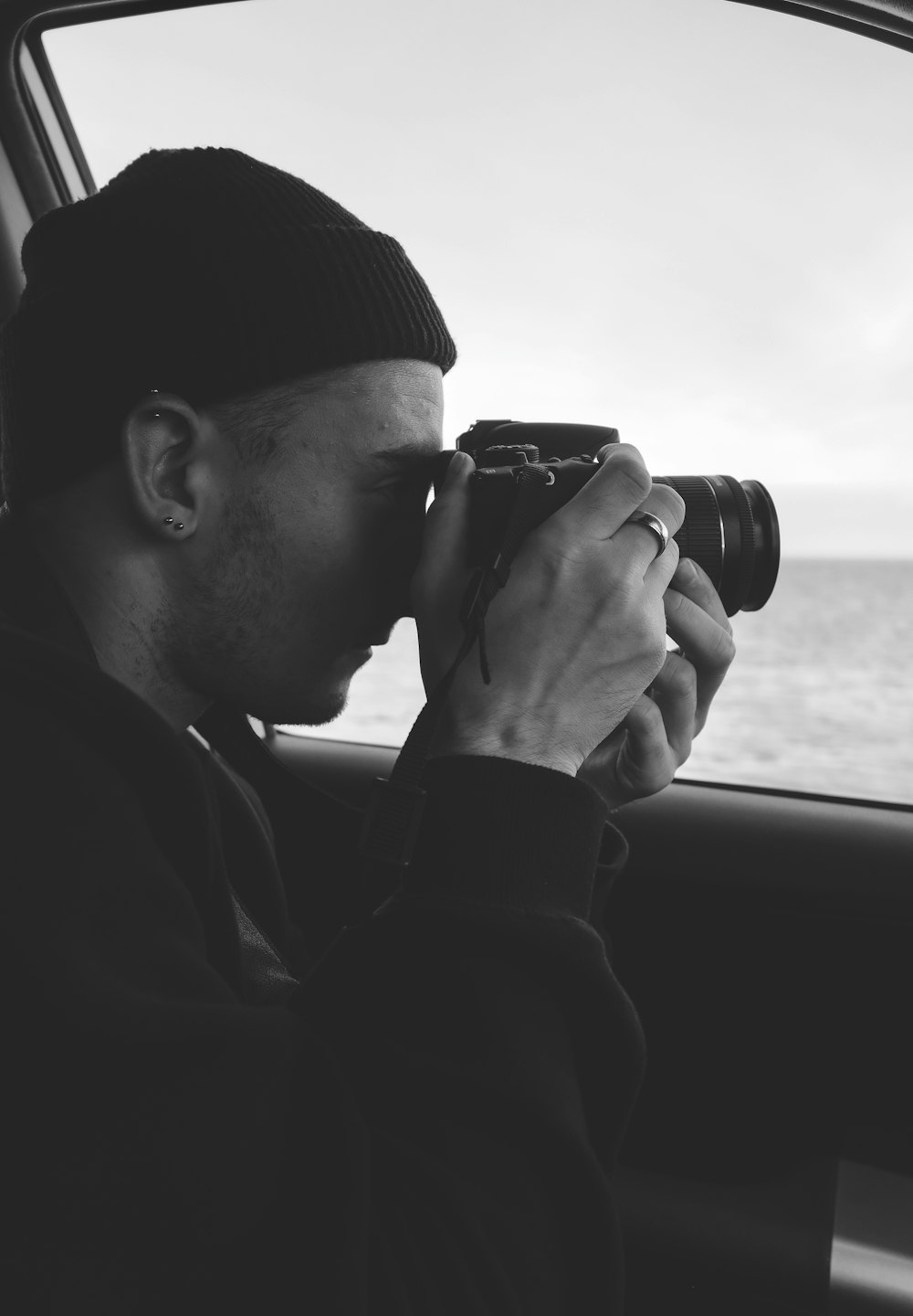 fotografía en escala de grises de un hombre sosteniendo una cámara DSLR