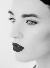 A close-up, black and white portrait of a woman's face highlights distinct features such as full lips with dark lipstick, expressive eyes, and well-defined eyebrows. The monochrome tones create a classic and elegant aesthetic.