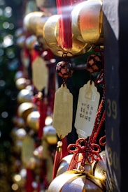 An arrangement of golden wind chimes with red tassels hanging vertically. The focus is on a brass plate with Chinese characters engraved on it. The background is slightly blurred, enhancing the reflective gold and the vibrant red colors.