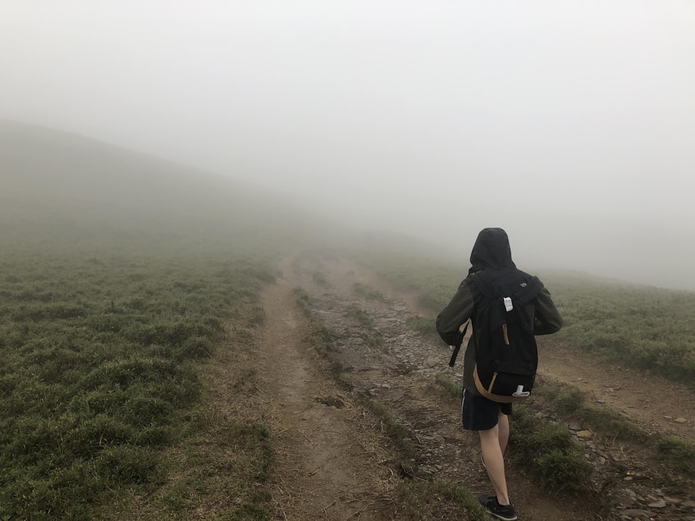 person carrying backpack while walking on green field