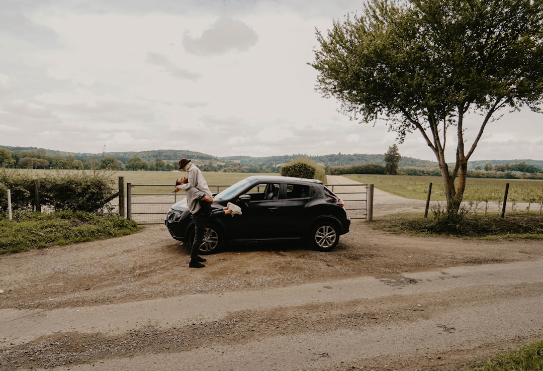 man lifting woman beside black Nissan Juke near tree