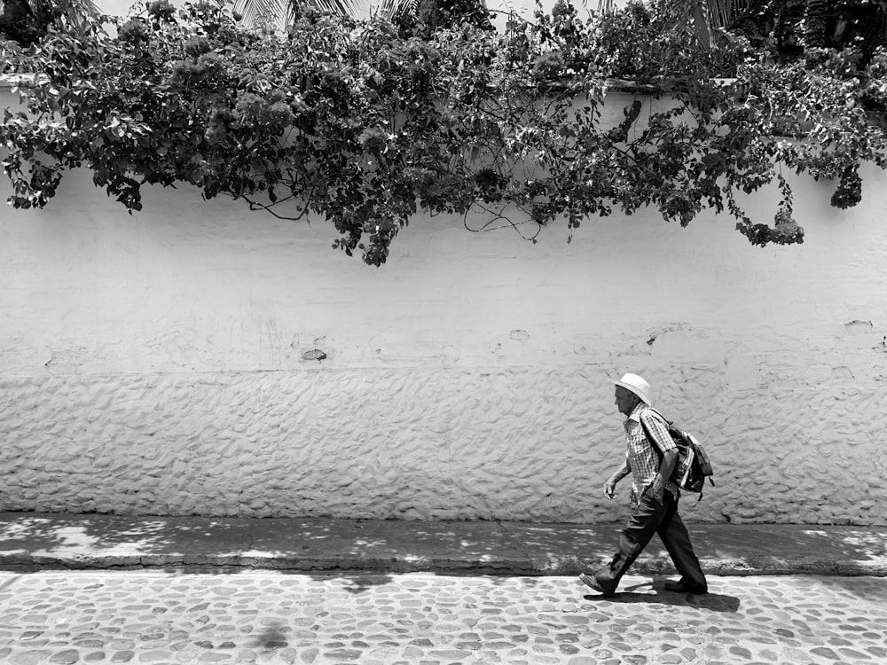 grayscale photography of man walking near tree