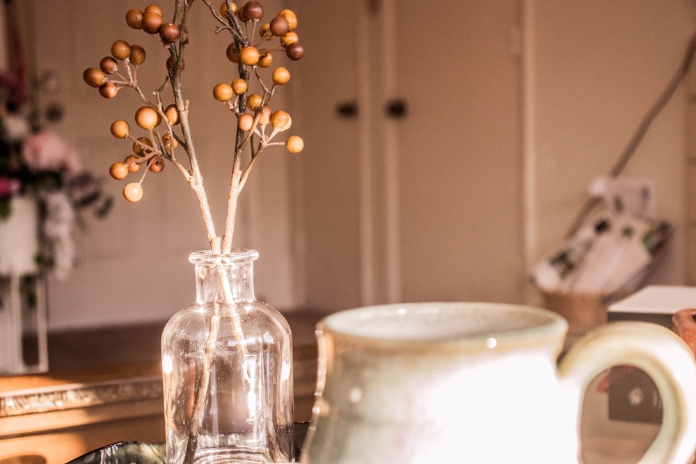 white ceramic mug near clear glass vase with brown flowers