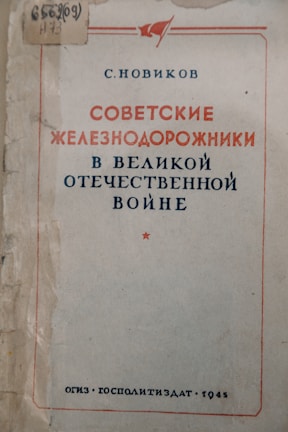 A vintage book cover with text in Russian, featuring red and blue typography. The edges of the cover show signs of wear, and there is a small red star below the title. There’s a decorative simple red banner at the top, and a library mark in the upper left-hand corner.