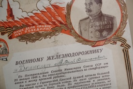 A vintage Soviet Union certificate featuring a detailed illustration of a military officer bordered by a laurel wreath. The officer is dressed in a decorated military uniform with medals. The design includes bold red and golden elements, like feathers and a tower, and text in Cyrillic script.