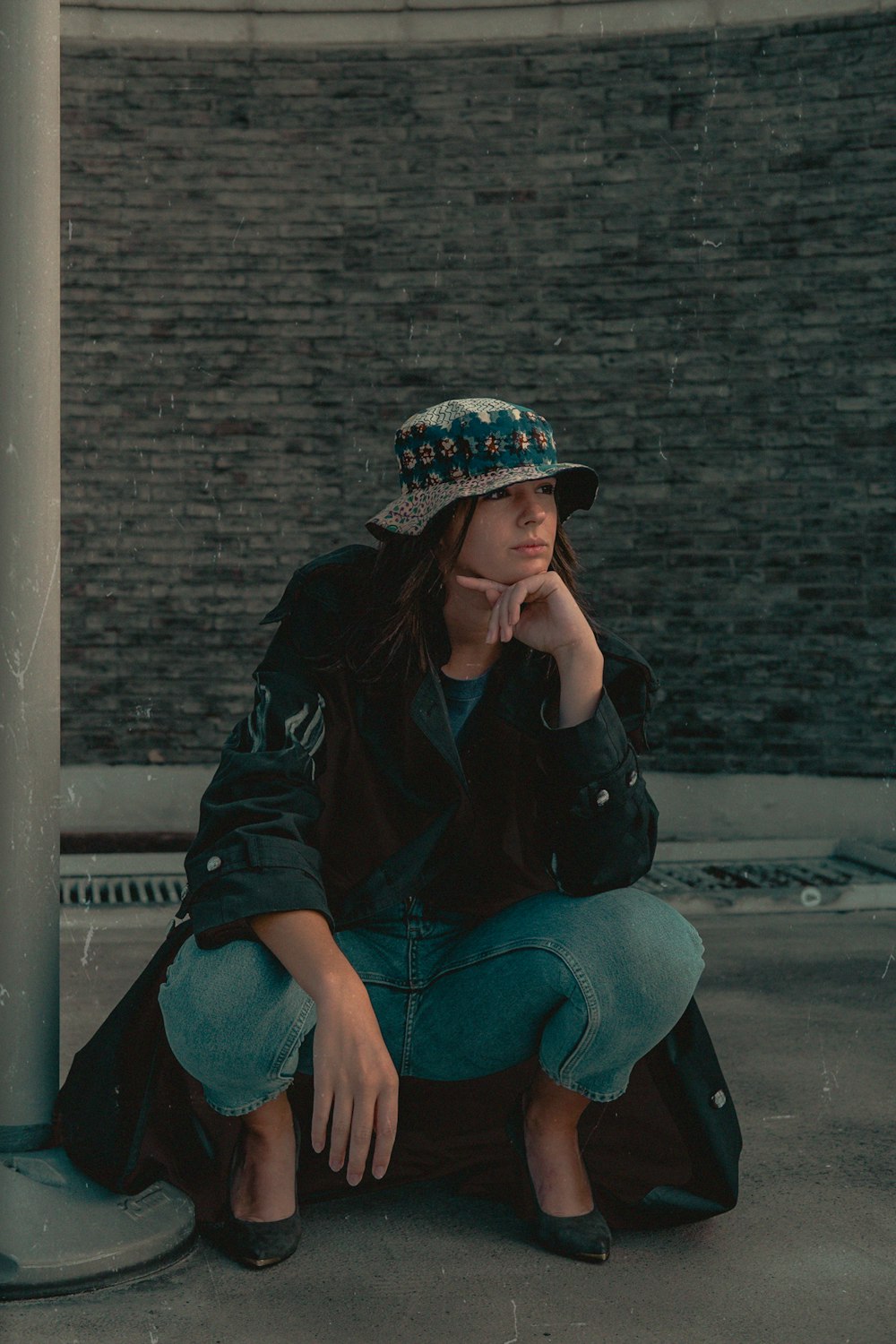 woman wearing black coat sitting beside gray metal post