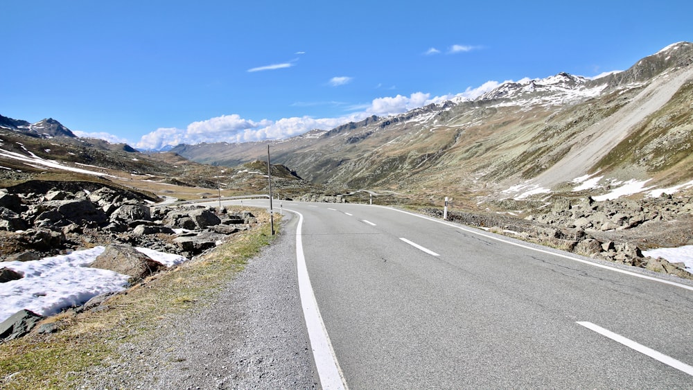 gray concrete road viewing mountain under blue and white skies during daytime