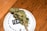A cannabis bud lying on a white circular lid with text around the edge, placed on a wooden surface.