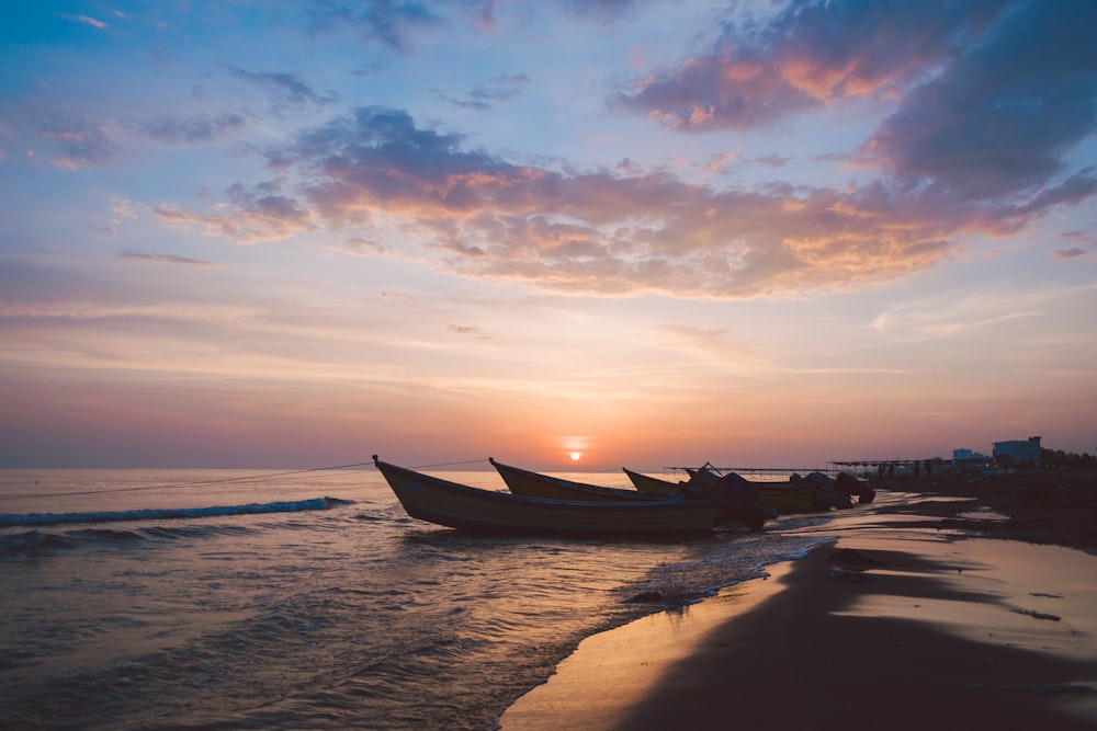 silhouette of boats on seashore under cloudy sky during golden hour