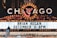 A brightly lit marquee advertising a performance by Brian Regan on December 31 at 8 PM. The marquee is part of a larger theater sign, adorned with numerous lights and a large, illuminated 'Chicago' sign at the top. A person is visible standing on a raised platform in front of the marquee.