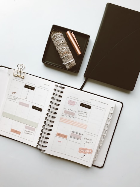 A neatly arranged flat lay of a colorful planner with a pen and a cup of coffee on a wooden desk.
