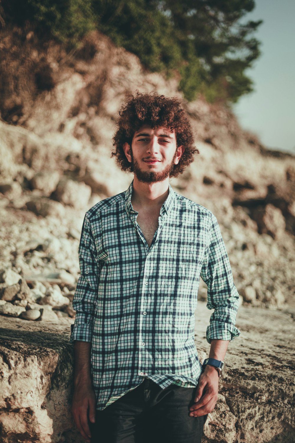 man in blue and black plaid long-sleeved shirt standing behind rock during daytime