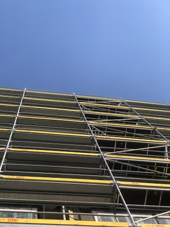 A close-up of sturdy steel scaffolding set up at a busy construction site under a clear blue sky.