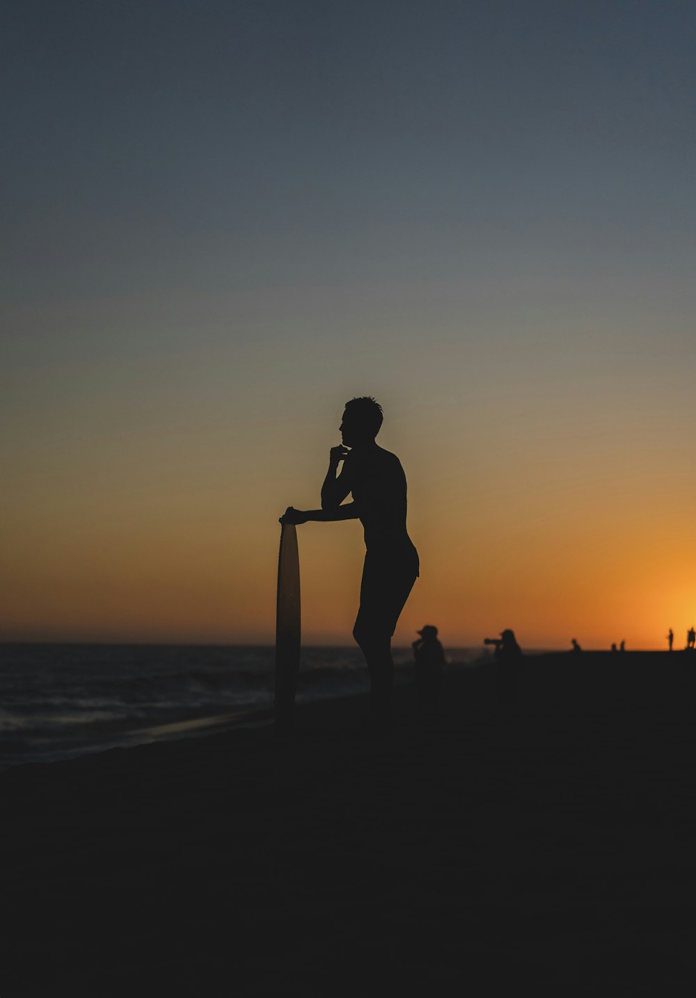 person standing and holding surfboard on shore during golden hour