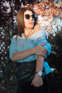 A stylish young woman wearing sleek black sunglasses and a gold watch, smiling confidently outdoors.