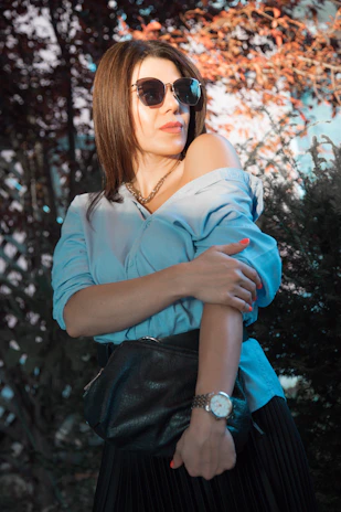 A stylish young woman wearing sleek black sunglasses and a gold watch, smiling confidently outdoors.