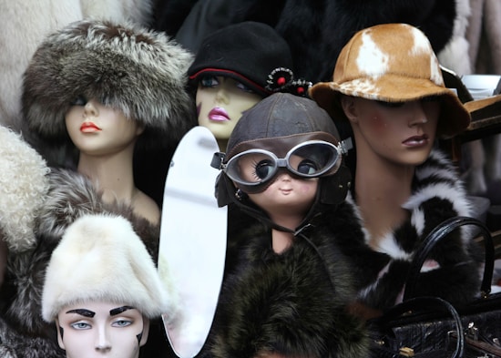 A collection of mannequin heads adorned with various hats and accessories. The hats are made from materials such as fur and leather, ranging from aviator goggles to wide-brimmed styles. Each mannequin exudes a unique character due to the distinct headwear choices, with some displaying elegant flower details and others a more vintage pilot look.
