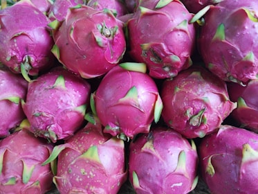 A cluster of dragon fruit with vibrant pink skin and green-tipped scales. The fruits are closely packed, displaying their unique texture and tropical appearance.