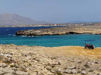 black and red motorcycle near seashore viewing blue sea during daytime