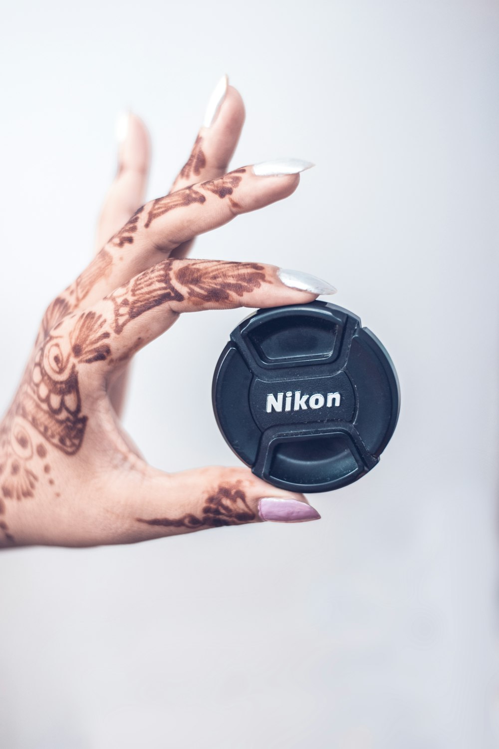 person holding black Nikon camera lens cover