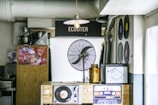 A small retro-themed room with vintage decor featuring vinyl records displayed on the wall, an old-school fan, and a wooden counter with a vinyl disc player. There are drink posters displayed on the wood panel and an amber glass bottle on the counter.