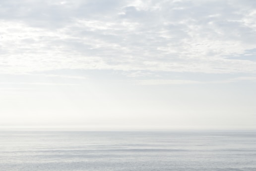 A tranquil seascape with soft, rippling waves stretching towards the horizon under a cloudy sky, creating a serene and peaceful atmosphere.
