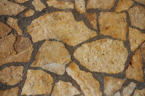 A close-up view of a stone wall featuring irregularly shaped, tan-colored stones set in dark mortar.