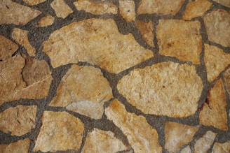 A close-up view of a stone wall featuring irregularly shaped, tan-colored stones set in dark mortar.