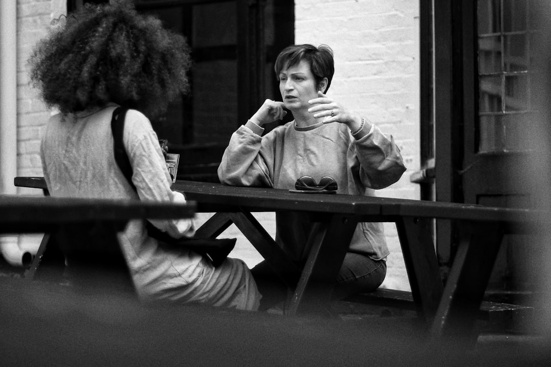 grayscale photo of two women sitting on bench, Convo.