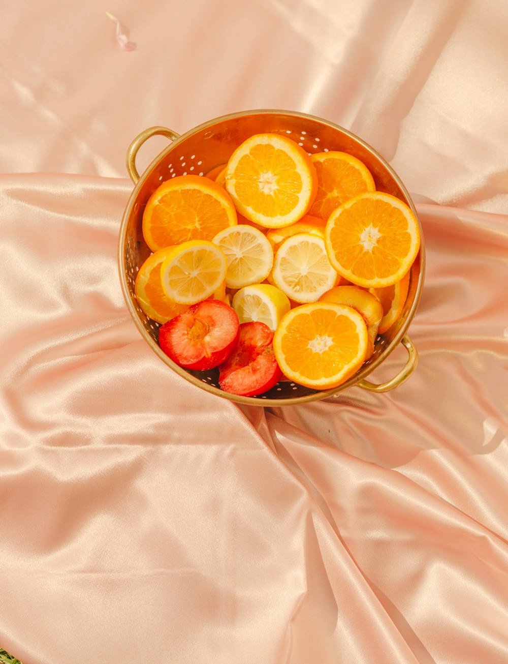 a bowl of sliced oranges and strawberries on a pink satin