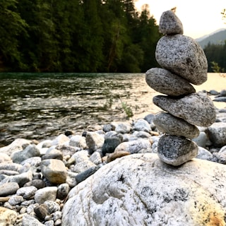 A minimalist scene of smooth stones stacked beside a calm river flowing through mountains.