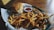 A plate filled with a generous serving of crispy golden fries accompanied by a hamburger with cheese, placed on a piece of white parchment. A small cup of ketchup sits beside the burger, all resting on a wooden table.