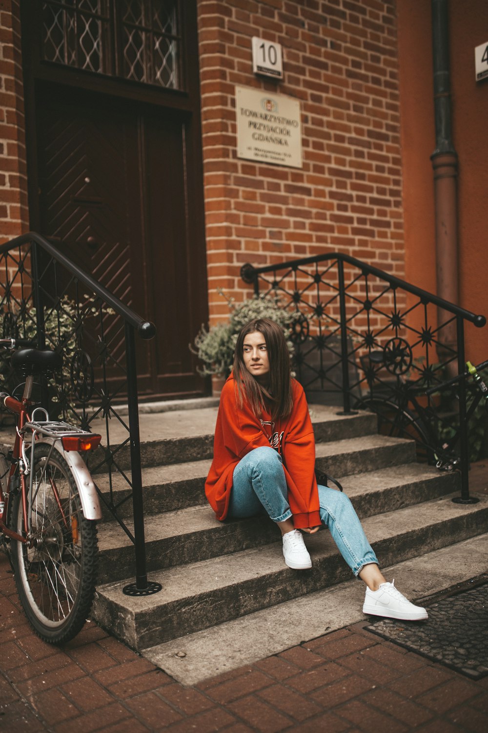 woman in red pullover hoodie sitting in front of closed door during daytime