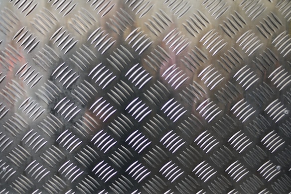 A textured metal surface with diamond-shaped patterns commonly found on industrial metal flooring or surfaces.