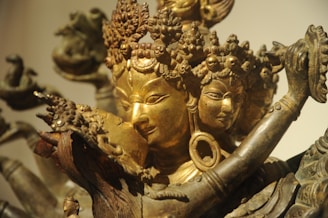 The image features a detailed sculpture of a multi-faced deity, intricately crafted with multiple hands holding various objects. The sculpture is adorned with elaborate headdresses and jewelry, showcasing fine artistry.