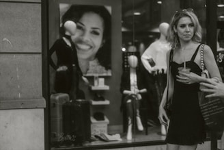 A chic woman in a classic black dress and pearl necklace, holding a coffee cup outside a stylish boutique.