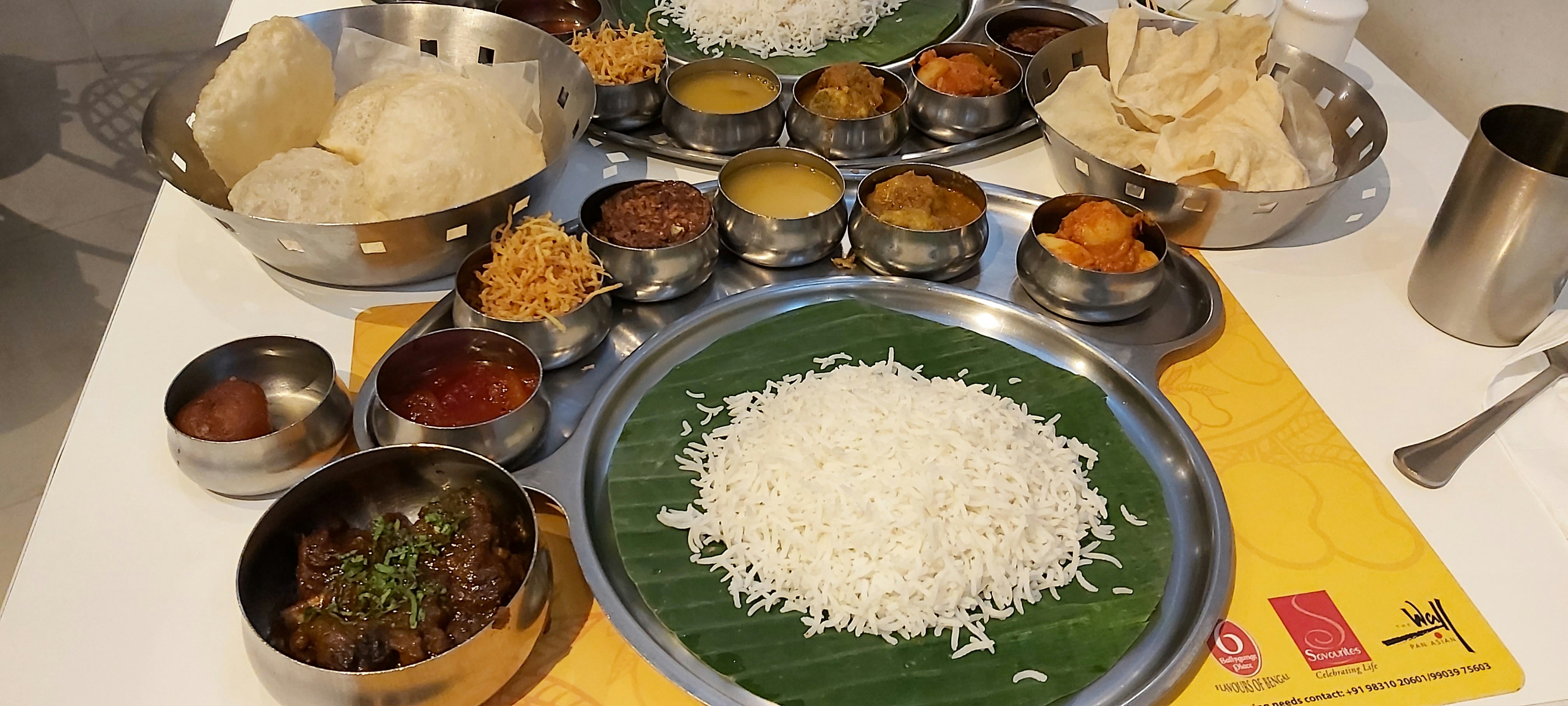 Full Konkani meals thali spread with multiple curries, rice and accompaniments — top view dark wood table