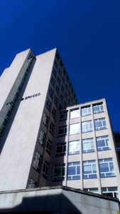 A tall, modern office building with multiple windows against a clear blue sky. The structure has clean lines and a minimalist design, with a sign that reads 'SPACES.' on the side. The building appears to be made of concrete or a similar material.