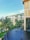 A modern luxury hotel with a contemporary architectural design features multiple stories with large glass windows and beige accents. Lush palm trees and well-maintained green gardens surround the building. The foreground showcases a tranquil infinity pool with a smooth, dark surface.