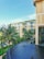 A modern luxury hotel with a contemporary architectural design features multiple stories with large glass windows and beige accents. Lush palm trees and well-maintained green gardens surround the building. The foreground showcases a tranquil infinity pool with a smooth, dark surface.