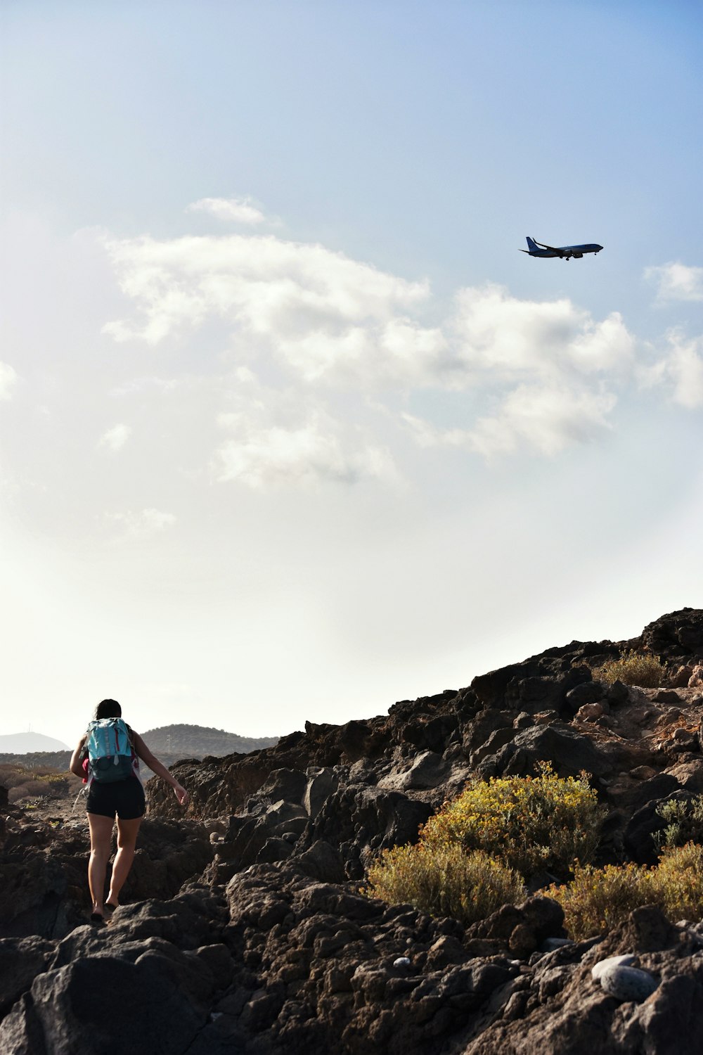 woman walking on rocks with airplane passing by
