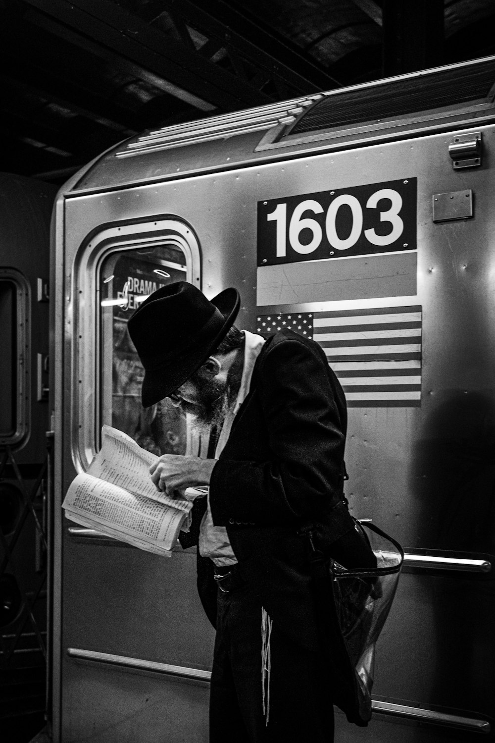 grayscale photo of man reading book beside train