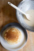 Hands pouring batter into a cast iron griddle, ready for pancakes.
