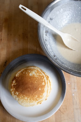 A cast iron griddle with golden pancakes stacked beside a cup of coffee.
