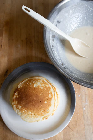 Hands pouring batter into a cast iron griddle, ready for pancakes.
