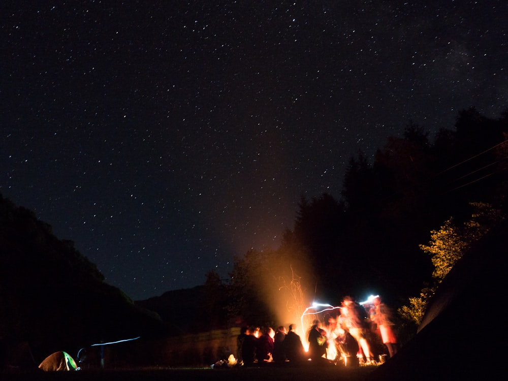 a group of people standing around a campfire at night